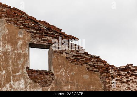 Un mur de briques avec un trou de fenêtre sur l'arrière-plan de ciel couvert Banque D'Images