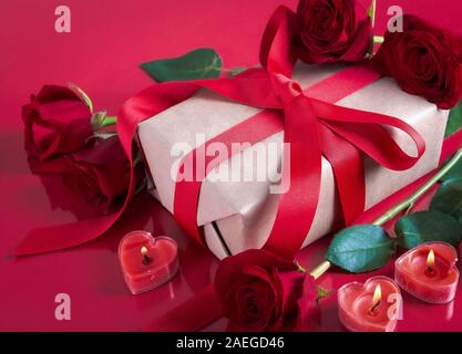 Cadeau de Saint-Valentin avec roses rouges en forme de coeur et de brûler des bougies sur une table réfléchissant rouge Banque D'Images