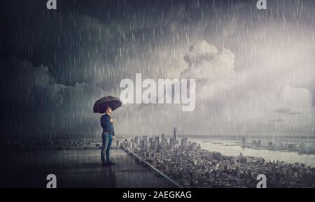 Thoughtful businessman standing under tempête sur le toit d'un gratte-ciel à regarder l'horizon de la ville. Concept de recherche d'affaires. Homme confiant le logement Banque D'Images