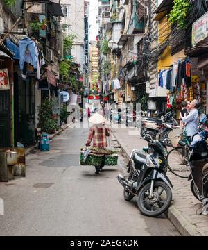 Vietnamienne portant chapeau conique la vente de légumes dans ruelle lane en moto, Hanoi, Vietnam Banque D'Images