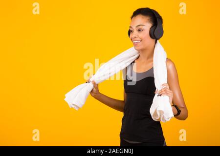 Black Girl in Headphones Holding Towel debout sur fond jaune Banque D'Images