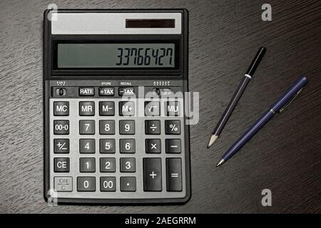 Calculatrice, stylo et crayon sur table bureau sombre. Vue de dessus. Banque D'Images