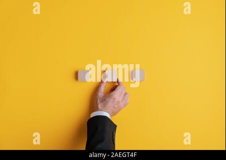 Main d'un businessman de placer trois blocs de bois dans une rangée sur fond jaune. Avec l'exemplaire de l'espace. Banque D'Images