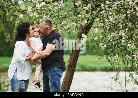 Embrassant l'enfant. Cheerful couple enjoying nice week-end en plein air avec sa petite-fille. Bon temps de printemps Banque D'Images