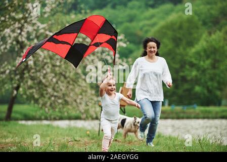 Jeu actif. Grand-mère et enfant féminins positifs avec l'exécution de couleur rouge et noir en kite hands outdoors Banque D'Images