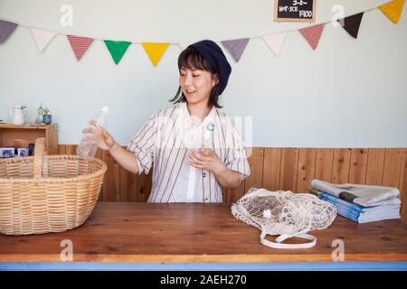 Japanese woman standing in a farm shop, le tri des bouteilles en plastique transparent en panier. Banque D'Images