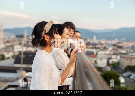 Groupe de jeunes hommes et femmes japonais debout sur un toit dans un milieu urbain. Banque D'Images