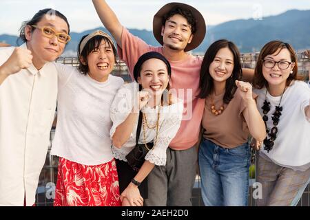 Smiling groupe de jeunes hommes et femmes japonais debout sur un toit dans un milieu urbain. Banque D'Images
