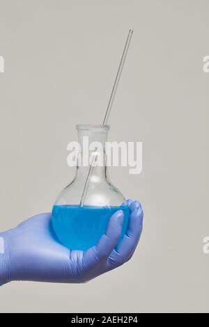 Close-up of male hands holding gants en fiole avec de l'eau bleu pendant expérience scientifique Banque D'Images