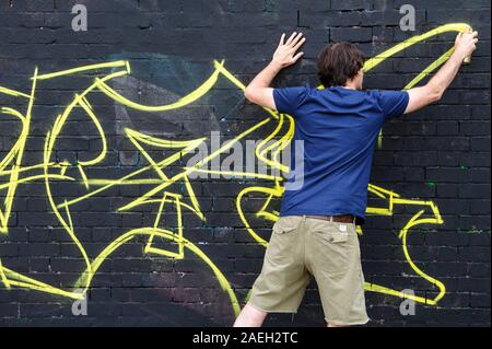 Artiste de graffiti masculin restant son propre dessin sur un noir mur Banque D'Images