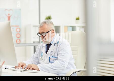 Maturité professionnelle médicale grave assis à la table et de travailler sur ordinateur à son bureau Banque D'Images