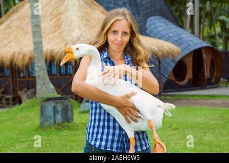 Jeune femme heureuse tenir en mains funny farm animal - Big White l'oie domestique. Journée de visite de la ferme sur la famille vacances d'été avec les enfants. Banque D'Images