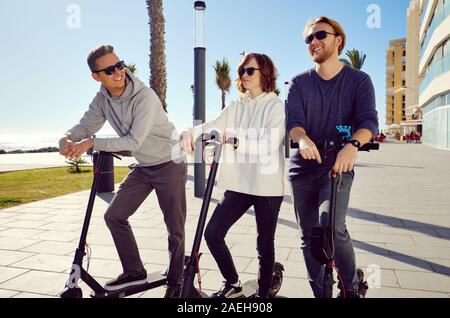 Trois meilleurs amis jeunes de 20 ans à 30 ans, fille et gars passent du temps à l'extérieur réunis ensemble à conduire sur un scooter électrique moderne véhicule terrestre Banque D'Images