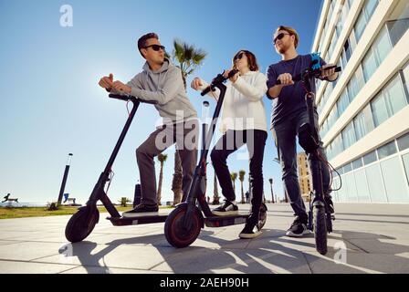 Trois meilleurs amis jeunes de 20 ans à 30 ans, fille et gars passent du temps à l'extérieur réunis ensemble à conduire sur un scooter électrique moderne véhicule terrestre Banque D'Images