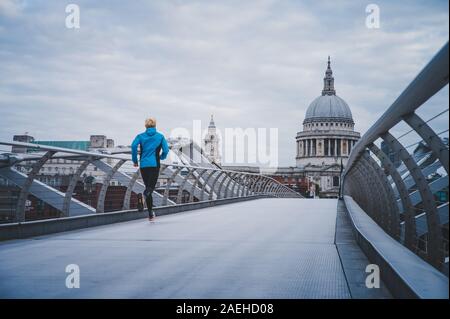 Jeune homme actif tournant au millénaire passerelle sur la Tamise, la Cathédrale St Paul en arrière-plan Banque D'Images