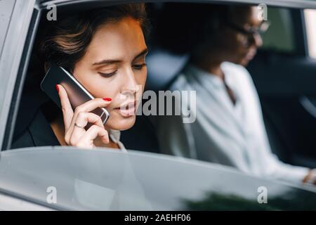 Businesswoman talking on a cell phone while sitting par une collègue dans un taxi Banque D'Images