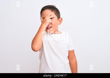 Bel enfant garçon portant des T-shirt debout sur fond blanc isolé avec des pics de shock couvrant le visage et les yeux avec la main, à la recherche à fi Banque D'Images