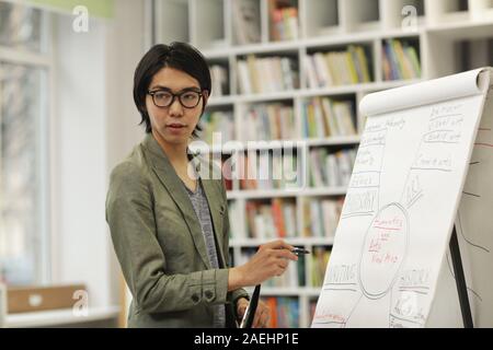 Portrait de jeune homme asiatique à lunettes debout près du tableau blanc et regardant la caméra au cours d'une présentation Banque D'Images