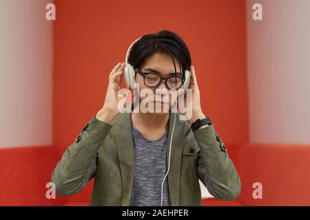 Jeune homme asiatique à lunettes portant des écouteurs et écouter de la musique avec fond orange Banque D'Images