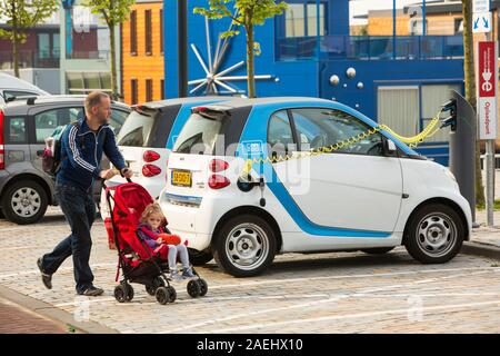 Une voiture Smart voiture électrique à une borne de recharge pour voitures électriques à Ijburg, Amsterdam, Pays-Bas, en face de maisons flottantes. Banque D'Images