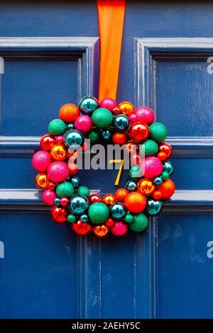 Couronne de Noël colorés faits de boules lumineuses accroché sur la porte avant en bois bleu avec le numéro de maison 7 Banque D'Images