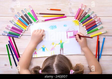 Un enfant tire une carte d'anniversaire avec sa famille. Dessin réalisé par un enfant avec des feutres et des crayons. Famille heureuse. Dessin d'enfant Banque D'Images