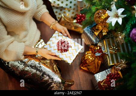 Gros plan sur femme élégante en robe d'or blanc et la jupe pour homme en vertu de l'arbre de Noël décoré des boîtes près de l'actuel livre enveloppé maintenant. Banque D'Images