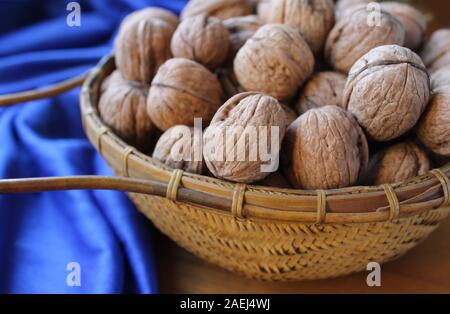 Un panier plein de noix en coquilles, en close up avec un fond bleu classique. Nature rustique de la nourriture. Banque D'Images