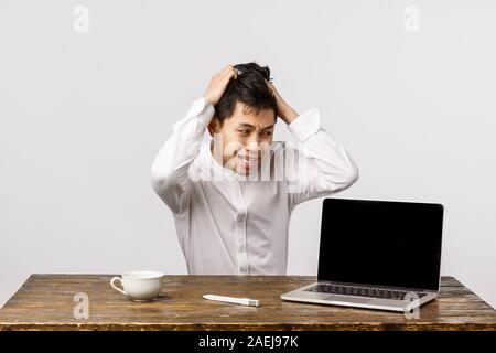 Alarmé et paniquer guy chinois tirant les cheveux de tête posée troublé et bouleversé, avoir problème énorme, regardant un ordinateur portable avec hâte, nerveux Banque D'Images