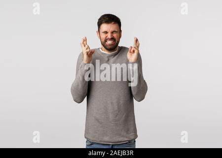 Excité et nerveux adultes barbu homme désireux de gagner la loterie, atteindre prix, dents et fermer les yeux de clench, traverser les doigts bonne chance, priant et veulent l'espoir Banque D'Images