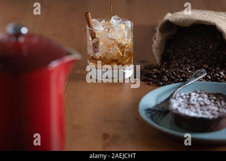 Préparer le café froid et verser dans un verre de glace pilée et un bâton de cannelle entouré par un sac de grains de café, gâteau et une presse française Banque D'Images