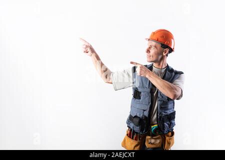 Le constructeur s'oriente vers la gauche. Offre avec l'index. Dans les vêtements de travail et casque de sécurité. Banque D'Images