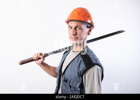 Un constructeur avec une grande épée sur son épaule. Réparateur portant un casque et des vêtements de travail. Banque D'Images