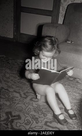 années 1950, historique, un enfant en bas âge assis sur un pot lisant un livre d'histoire. Banque D'Images