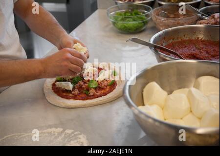 La préparation de Pizza Margherita sur une en haut. Morceaux de saucisse met pizzaiolo, mozzarella et basilic Feuilles sur une matière première, la pâte à pizza avec la sauce tomate. Banque D'Images