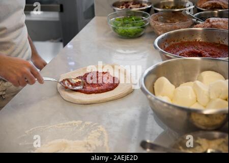 La préparation de Pizza Margherita sur une en haut. Pizzaiolo met de la sauce tomate sur une pâte à pizza de matières premières. Focus sélectif. Banque D'Images