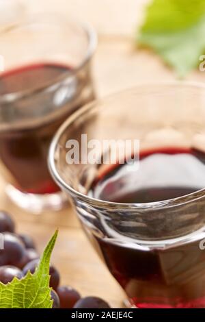 Deux verres à vin sans pied sur une table remplie de vin rouge, le raisin bleu et vert feuilles de raisin. L'angle vertical dutch avec focus sélectif, Banque D'Images