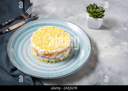 Mimosa salade russe traditionnelle avec la sardine, oignon, pomme de terre, carotte, fromage, oeufs et de la mayonnaise sur table béton Banque D'Images