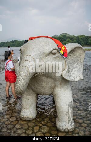 Guilin, Chine - Août 2019 : Chinese girl sécher sa serviette sur le haut de la grande statue de l'éléphant de marbre à côté du monument d'éléphant un Banque D'Images