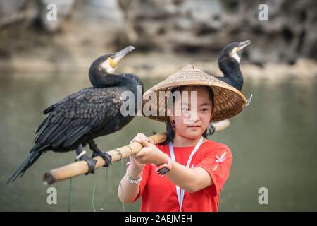 Guilin, Chine - Août 2019 : cute little girl holding chinois bâton de bambou avec des aigrettes d'oiseaux et de pose pour photo souvenir devant le landma Banque D'Images