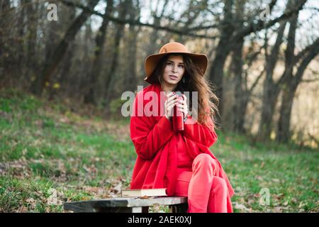 Portrait de jeune fille automne rouge attente thermos. Belle jeune brunette porte un manteau rouge, marron foulard et chapeau à large bord. Banque D'Images