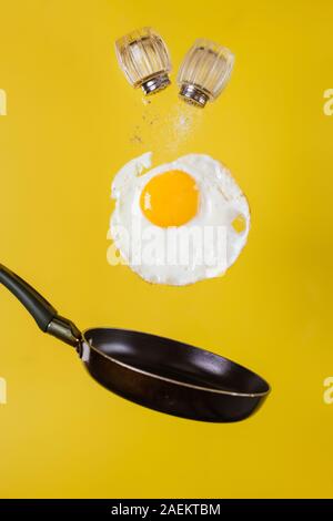 L'heure du petit-déjeuner. Un œuf frit et une poêle avec salières léviter dans l'air sur un fond jaune Banque D'Images