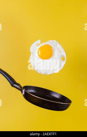 L'heure du petit-déjeuner. Un œuf frit et une poêle faire léviter dans l'air sur un fond jaune. Banque D'Images