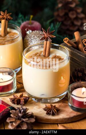 Un gros plan d'un verre de lait de poule avec un autre verre de lait de poule à l'arrière et entouré par des ornements, des bâtons de cannelle, les bougies et l'anis étoilé. Banque D'Images