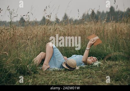 Femme couchée sur sac en champ et profiter de la lecture de livres. Banque D'Images