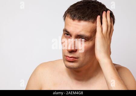 Brunette homme avec des ecchymoses sur son corps tient sa main à sa tête et se tord de douleur sur un arrière-plan blanc isolé. La santé et de la médecine. Banque D'Images