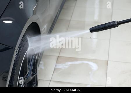 Un travailleur masculin se lave d'un disque de roue de voiture noire avec un appareil à haute pression où l'eau et élimine la mousse et les produits chimiques dans un véhicule d Banque D'Images