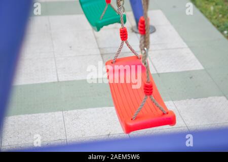 Et en plastique rouge et vert vide dans la chaîne des balançoires balançoires pour les enfants. chain suspendu dans le jardin. Childs swing dans un parc . Banque D'Images