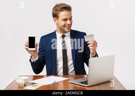 Attractive businessman en costume classique assis, en collaboration avec ordinateur portable, rapport écrit, après avoir briser commander en ligne, souriant, heureux holding credit Banque D'Images