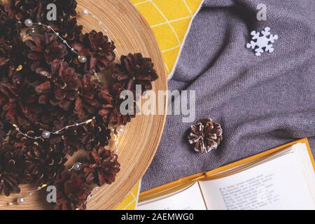 Composition de Noël avec livre ouvert avec l'hiver plaid douillet, les lumières de Noël en pommes de pin. Maison de vacances confort matin concept. Hygge style. Télévision lay, t Banque D'Images